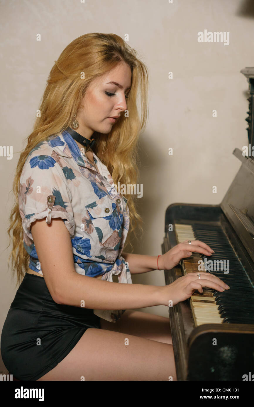 schönes blondes Mädchen mit offenen Haaren ist auf dem Klavier spielen. Stockfoto