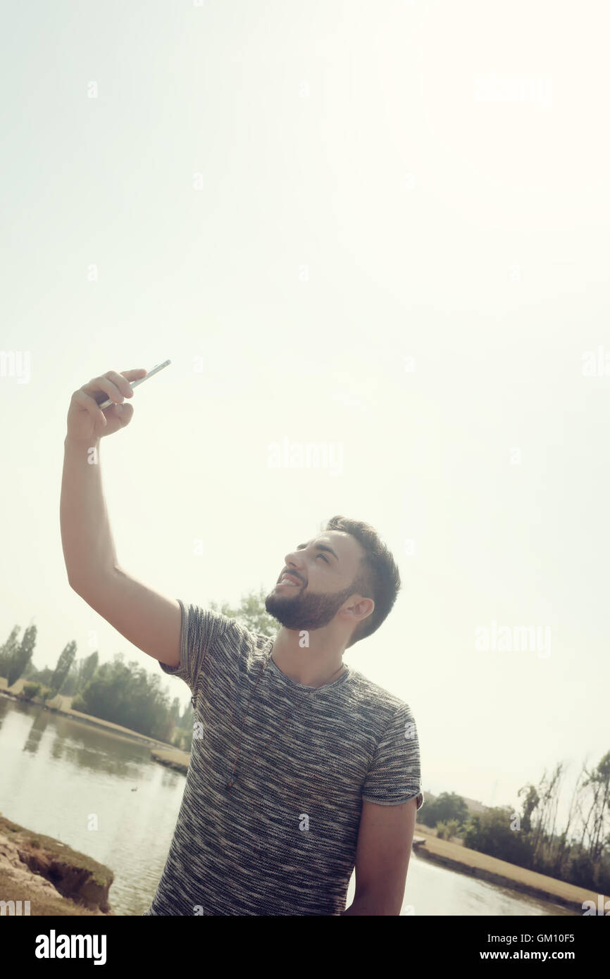 Junger Mann im Park mit Smartphone nimmt ein Selbstporträt. Stockfoto