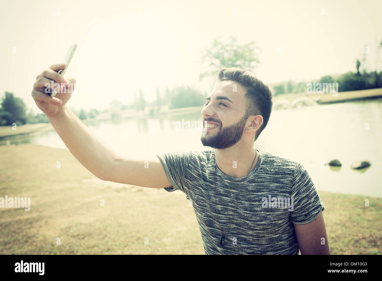 Junger Mann im Park mit Smartphone nimmt ein Selbstporträt. Stockfoto