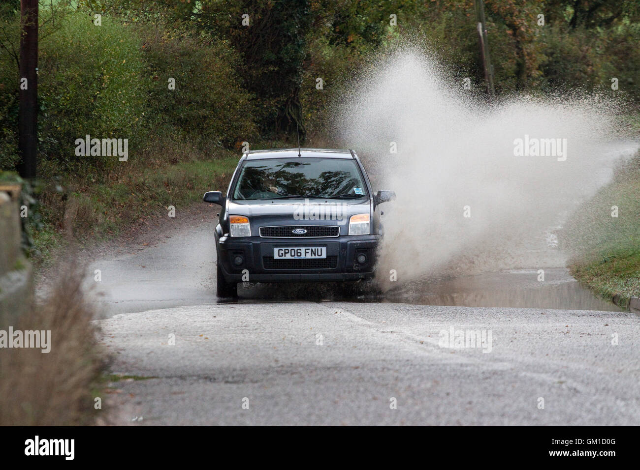 Limousine verursacht dramatische Spray, wie es durch eine leicht überfluteten Landstraße fährt Stockfoto