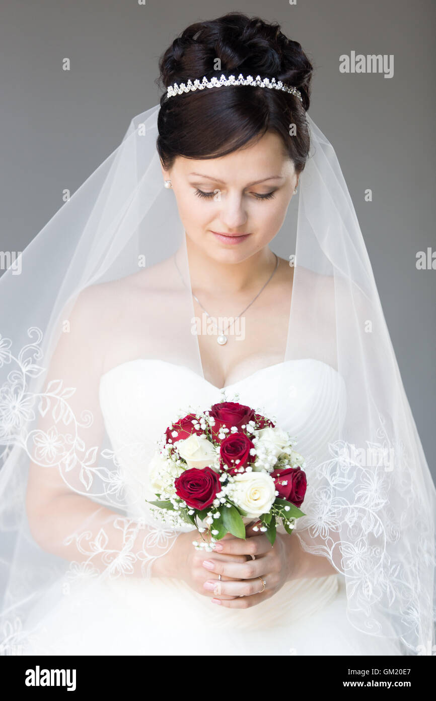 Porträt des jungen schönen Braut posiert mit ihren Augen nach unten, halten Brautstrauß mit weißen und roten Rosen. Attraktive Braut Stockfoto