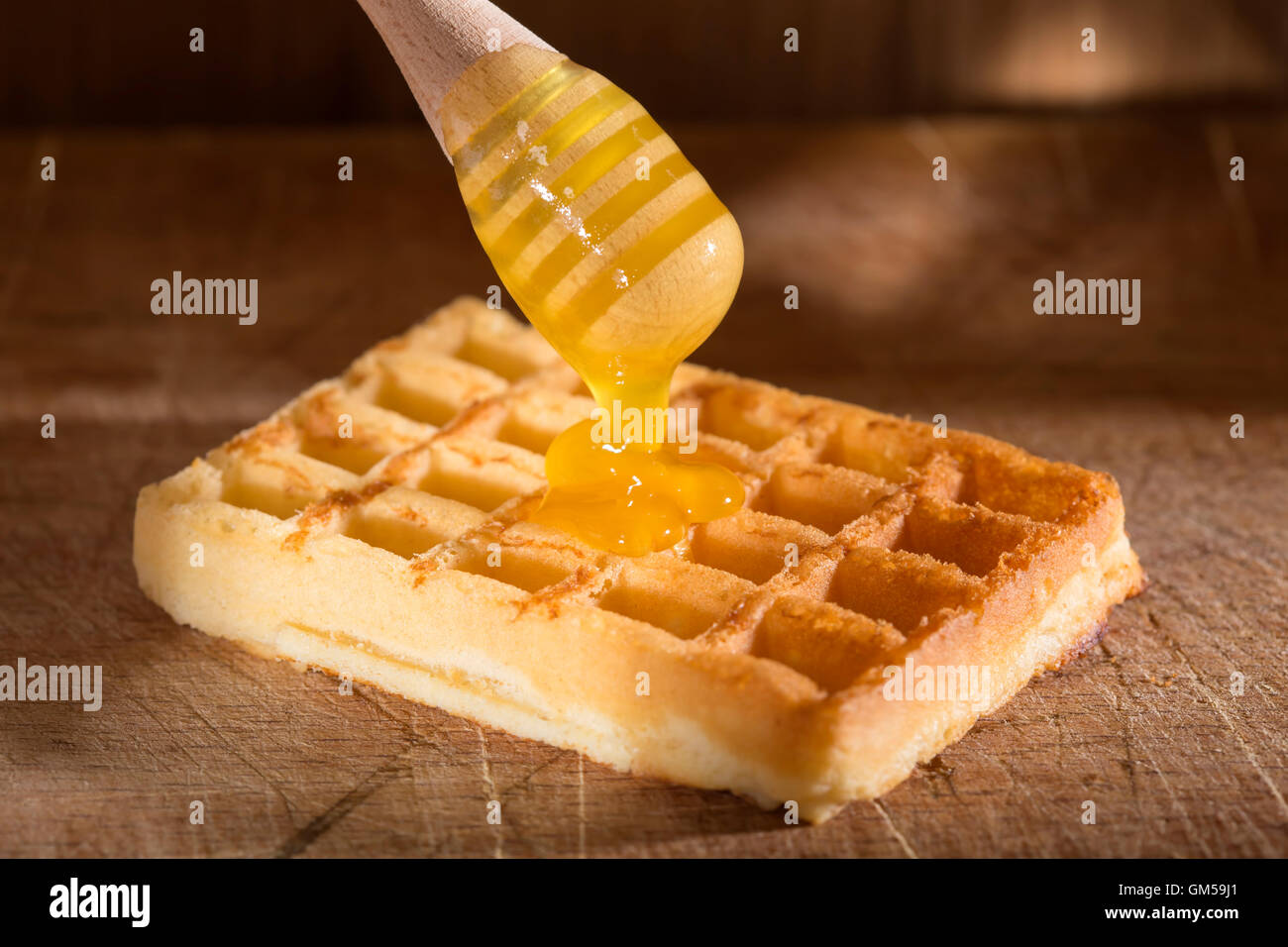 Honig, Gießen auf einer frischen Waffeln über hölzerne Hintergrund Stockfoto