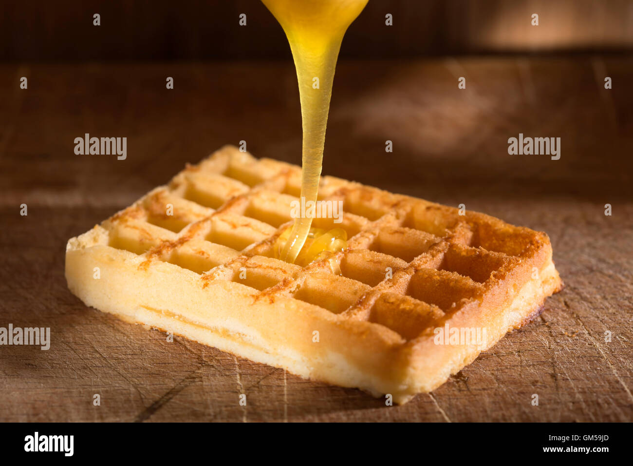 Honig, Gießen auf einer frischen Waffeln über hölzerne Hintergrund Stockfoto