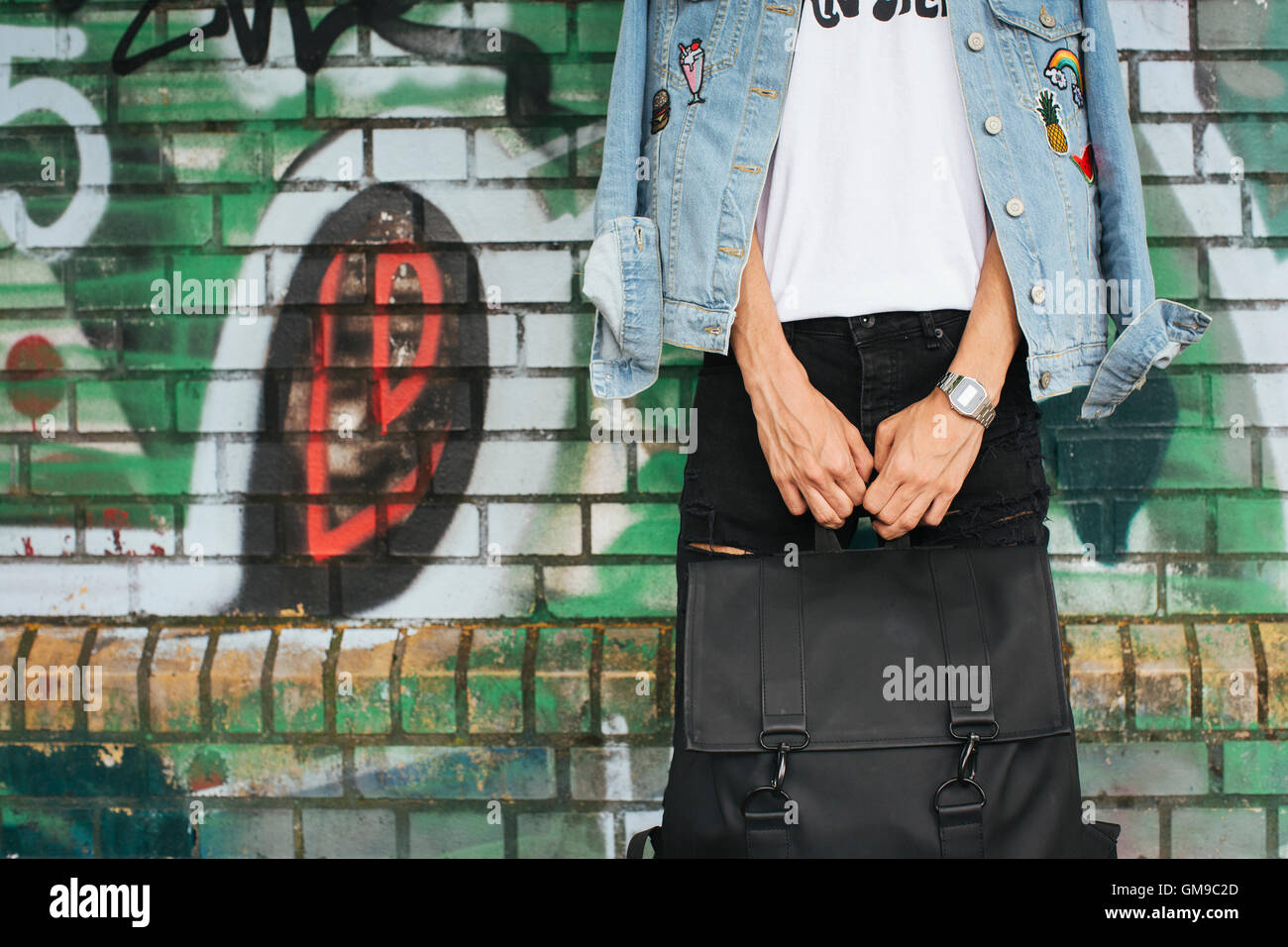 Junger Mann in Jeansjacke hält schwarze Tasche Stockfoto