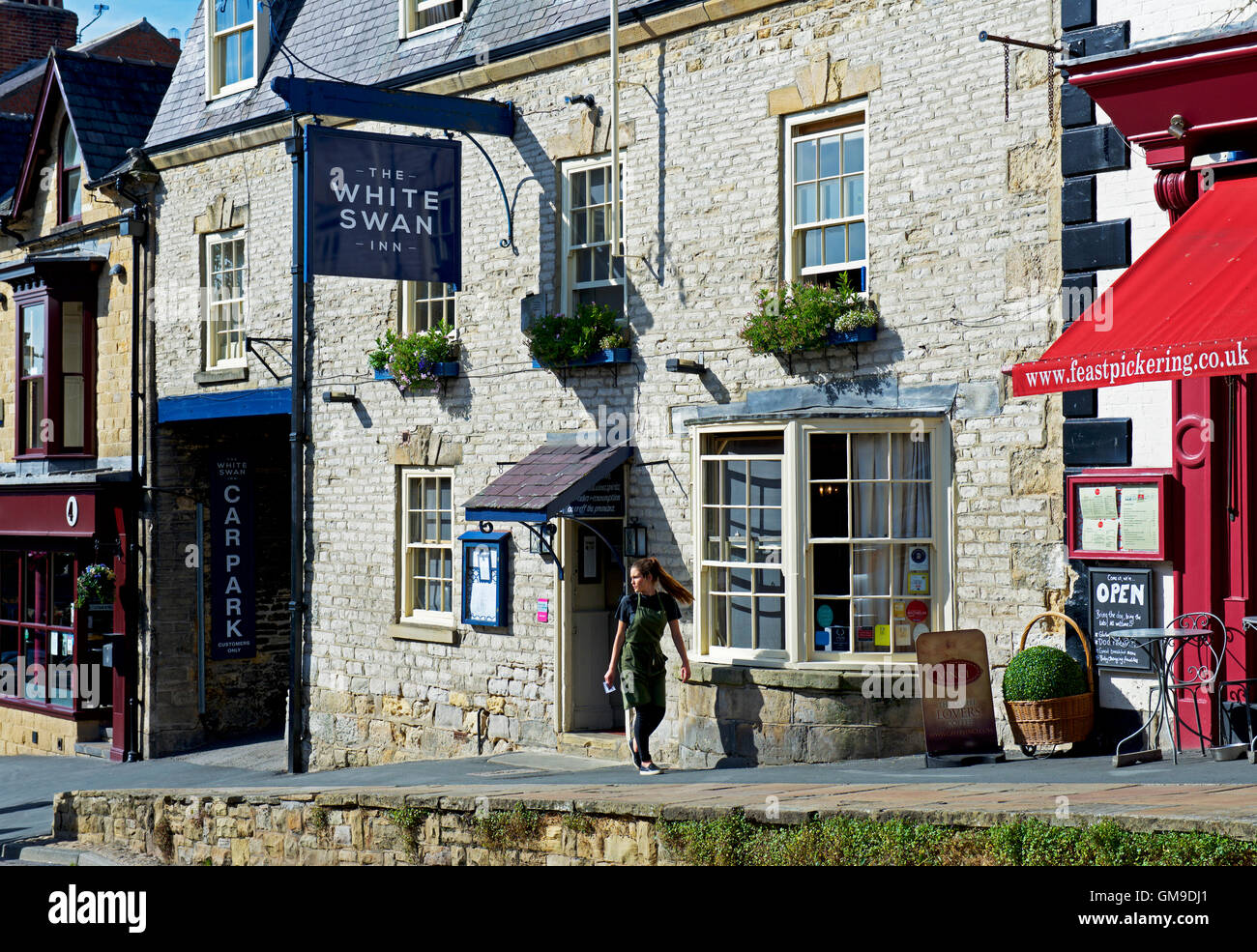 Junge Frau zu Fuß vorbei an der White Swan-Kneipe in Pickering, North Yorkshire, England UK Stockfoto