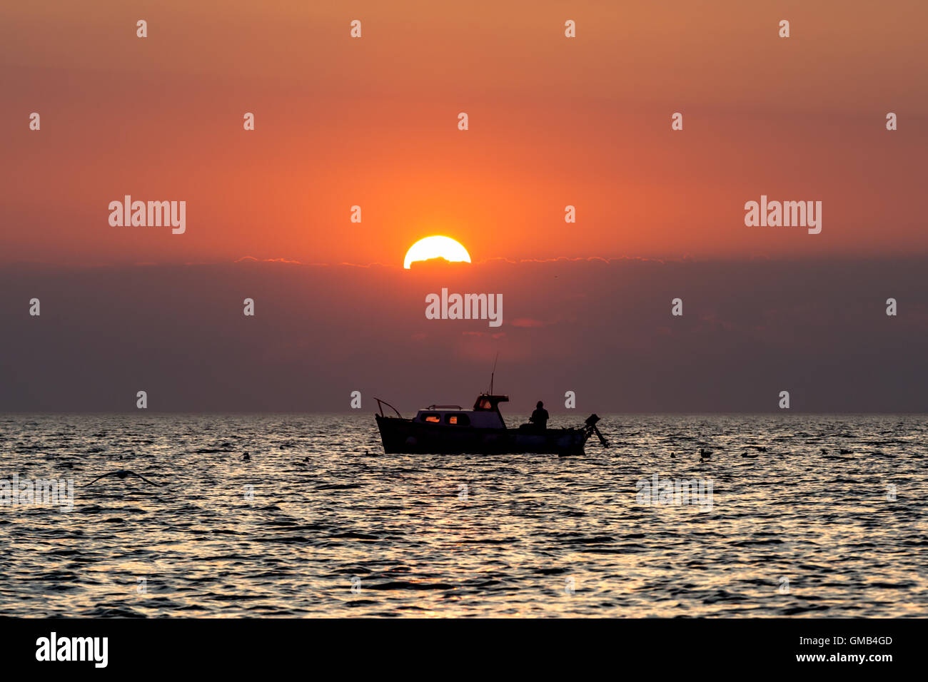 A Mann Angeln seines Bootes bei Sonnenuntergang, während in der Cardigan Bay verankert Stockfoto