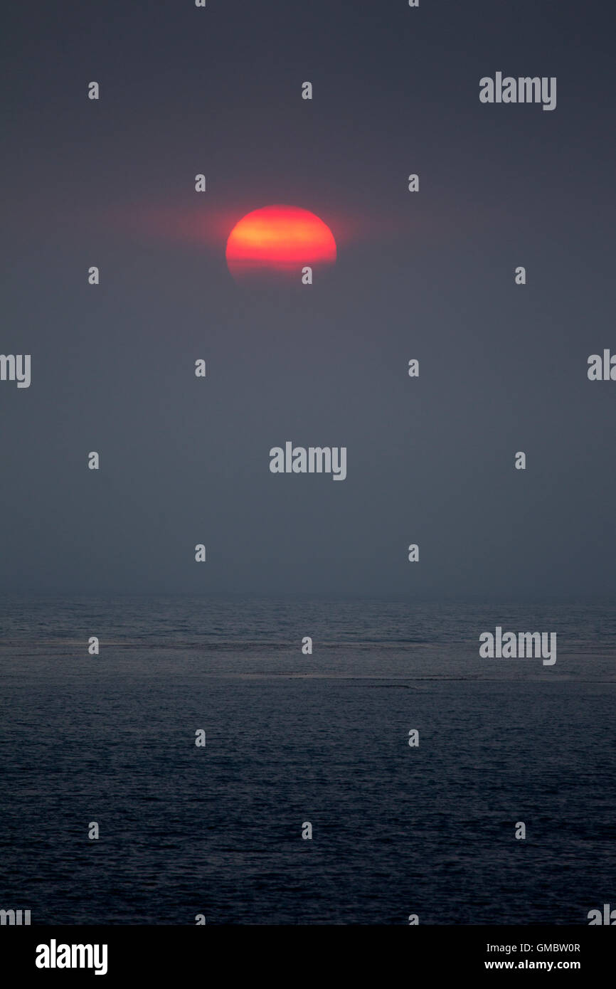 Rot gelb Sonne teilweise verdeckt durch Nebel über dem Ozean Stockfoto
