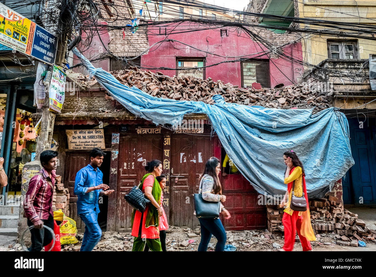 Ein Jahr nach den Erdbeben von 2015 gehen Bürger von Kathmandu vor einem Gebäude mit Trümmern in der Gegend von Thamel, Kathmandu, Nepal. Stockfoto