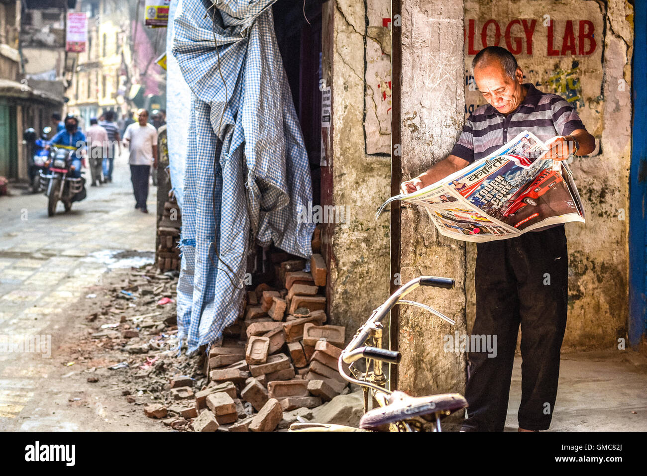 Ein Mann liest Zeitung in der Nähe eines Ruinenstapels in Thamel, Kathmandu, Nepal. Stockfoto