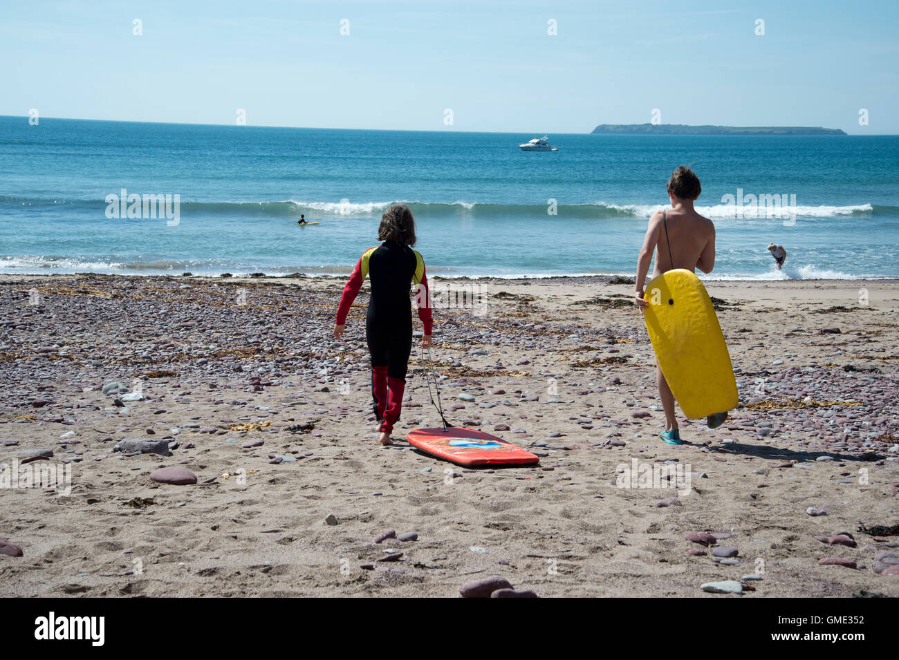Dale, Wales, August 2016. Zwei jungen gehen einen Neoprenanzug tragen in Richtung Meer mit Bodyboards. Stockfoto