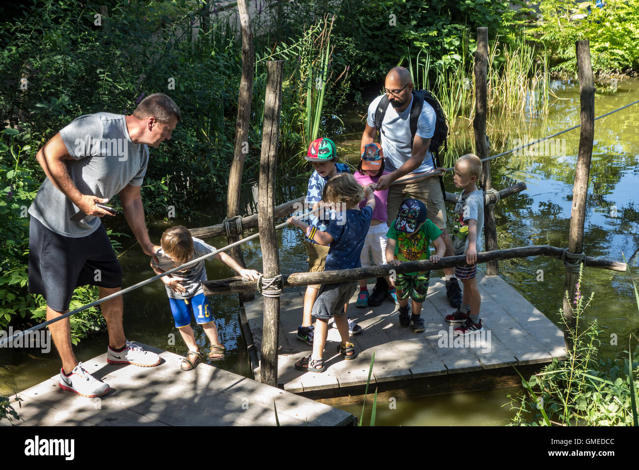 Eltern helfen, Kinder verlassen hölzerne Floß im Abenteuerpark für Kinder im Sommer Stockfoto