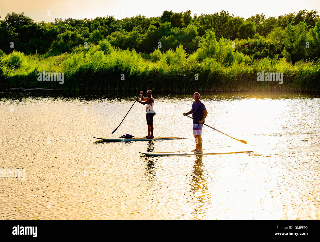 Zwei kaukasischen Männer mittleren Alters Ruder Stand-up Paddleboards entlang der North Canadian River. Sonnenuntergang Blendung, Oklahoma, USA. Stockfoto
