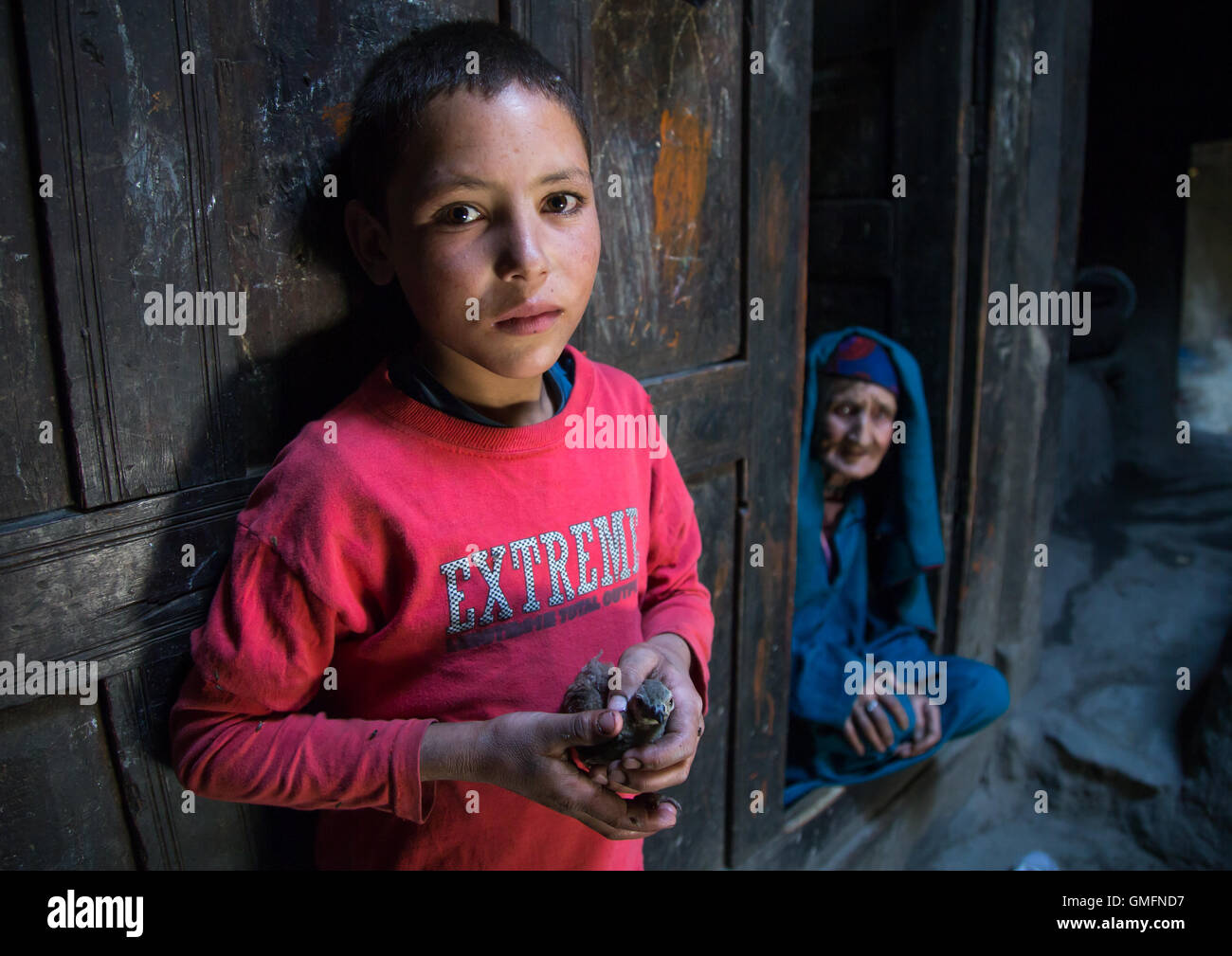 Afghanischer Junge hält einen Vogel in seine Hände und seine Großmutter im Haus Pamiri, Provinz Badakhshan, Qazi Deh, Afghanistan Stockfoto