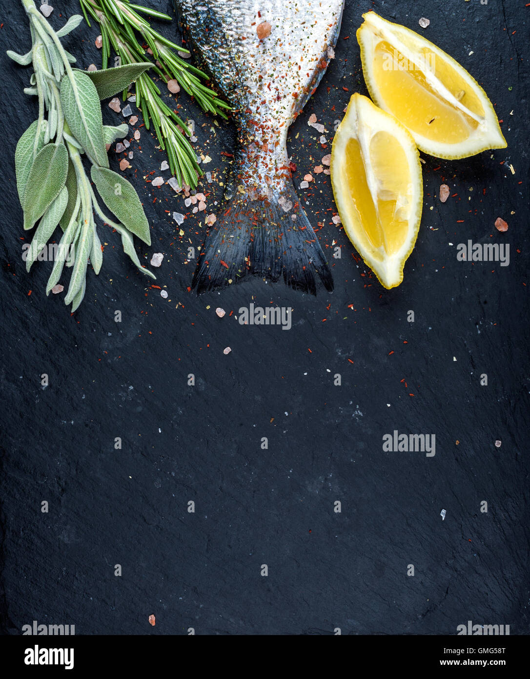 Heck des frischen rohen Dorado oder Dorade Fisch auf schwarzem Schiefer Steinplatte mit Gewürzen, Kräutern, Zitrone und Salz Stockfoto