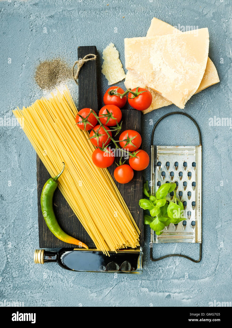 Zutaten für das Kochen von Teigwaren. Spaghetti, Parmesan-Käse, Cherry-Tomaten, Metall Reibe, Olivenöl und frischem Basilikum auf konkrete Hintergrund grau-blau Stockfoto