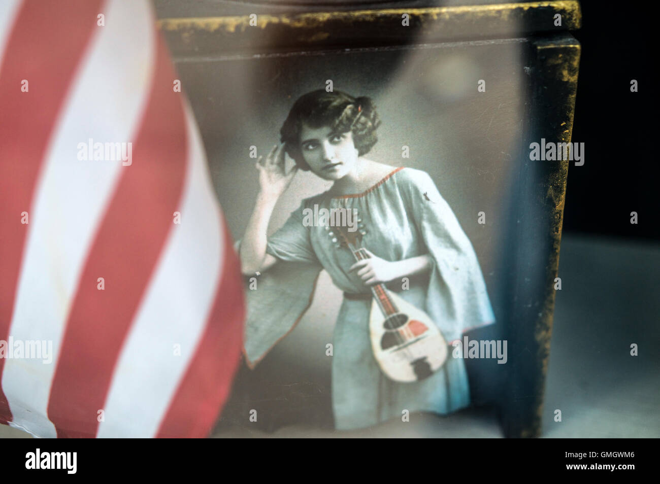 Eine Frau der 1920er Jahre in Tracht hält eine Mandoline hält ihre Hand anhören von Musik neben der amerikanischen Flagge Stockfoto