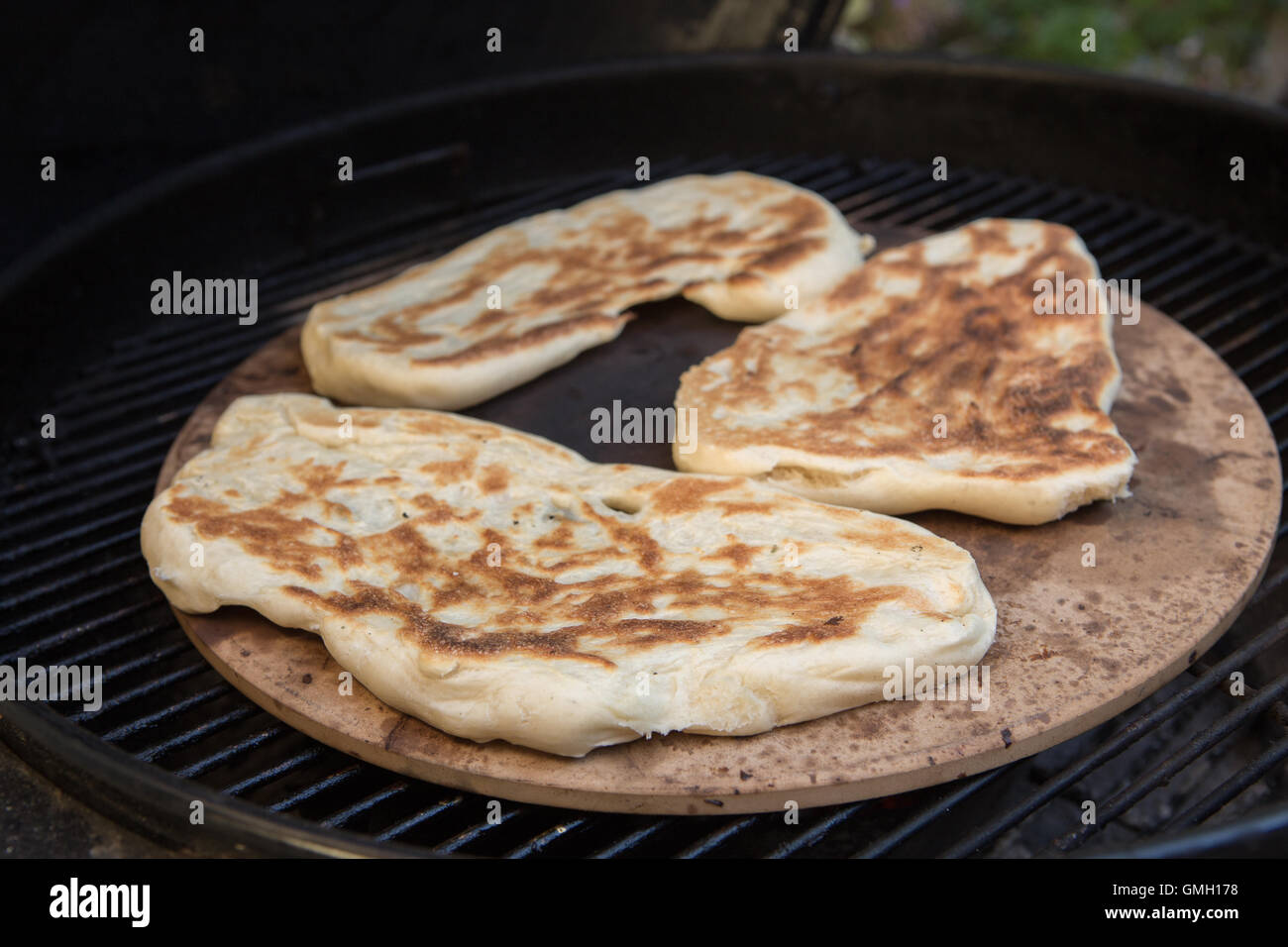 Frische hausgemachte Naan-Brot im Freien auf einem Pizzastein über einen Holzkohlegrill gegart Stockfoto