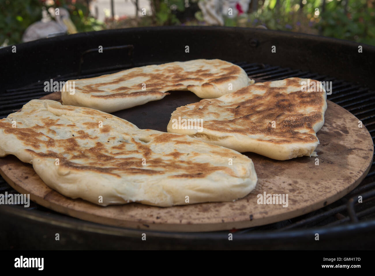 Frische hausgemachte Naan-Brot im Freien auf einem Pizzastein über einen Holzkohlegrill gegart Stockfoto