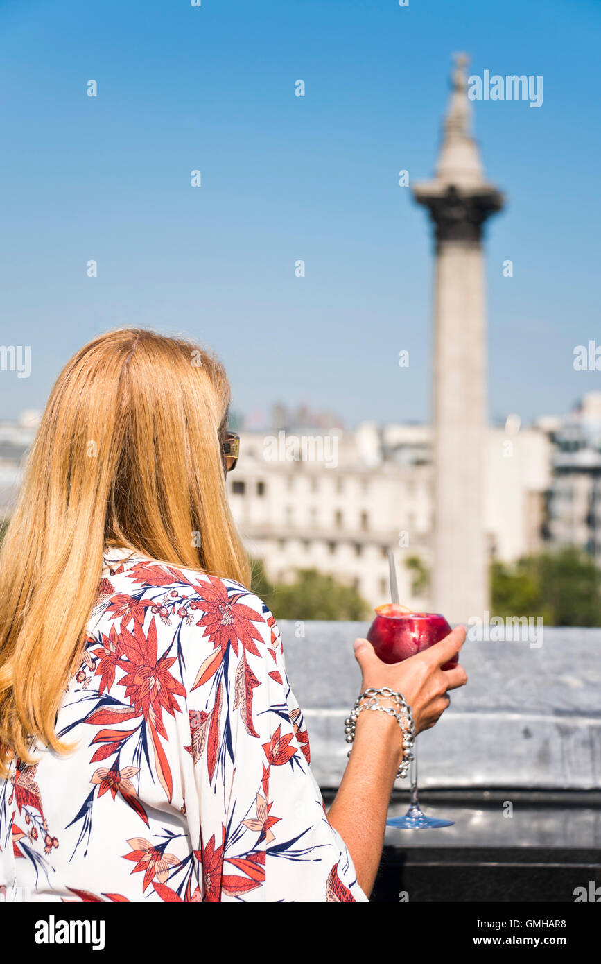 Vertikale Porträt einer Frau, die einen cocktail mit Blick auf Nelson Säule am Trafalgar Square in London, in der Sonne zu genießen. Stockfoto