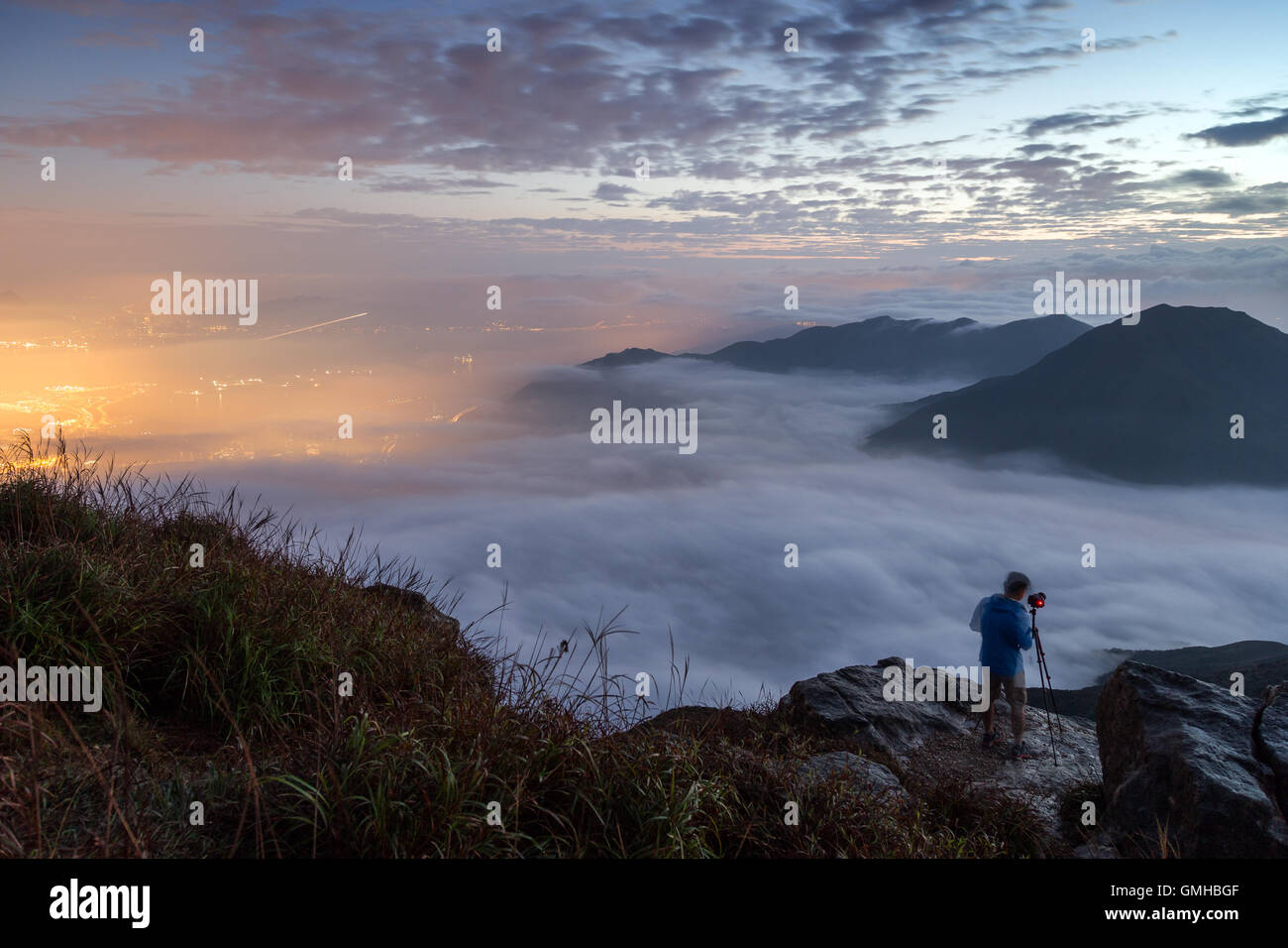Mann, die Lichter der Tung Chung Neustadt unter Wolken auf Lantau Island in Hongkong zu fotografieren. In der Morgendämmerung betrachtet von Lantau Peak. Stockfoto