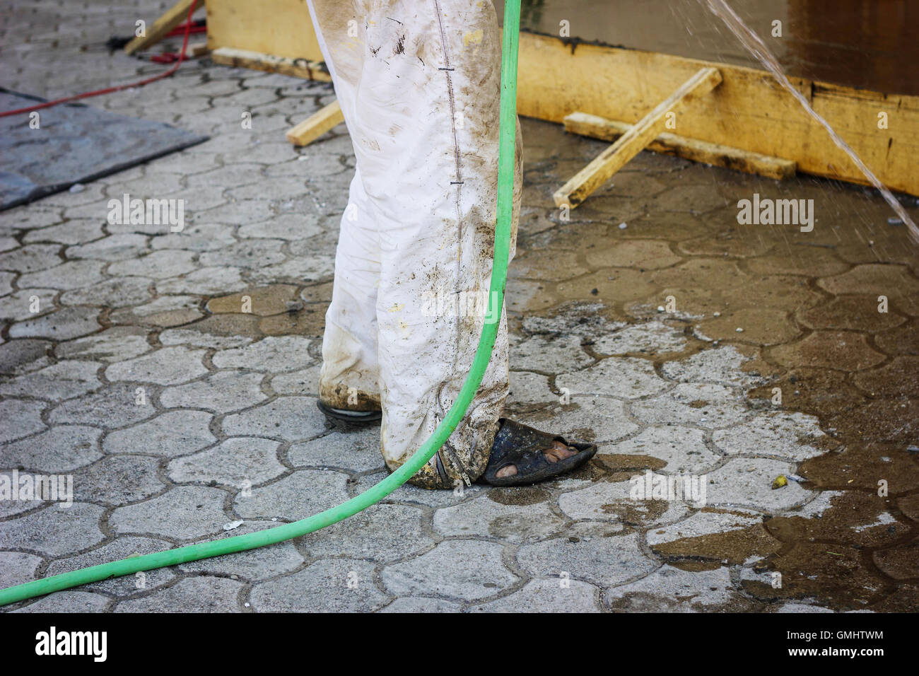 schmutzige Füße des Arbeitnehmers mit Sandalen stehen mit dem Wasserschlauch Stockfoto