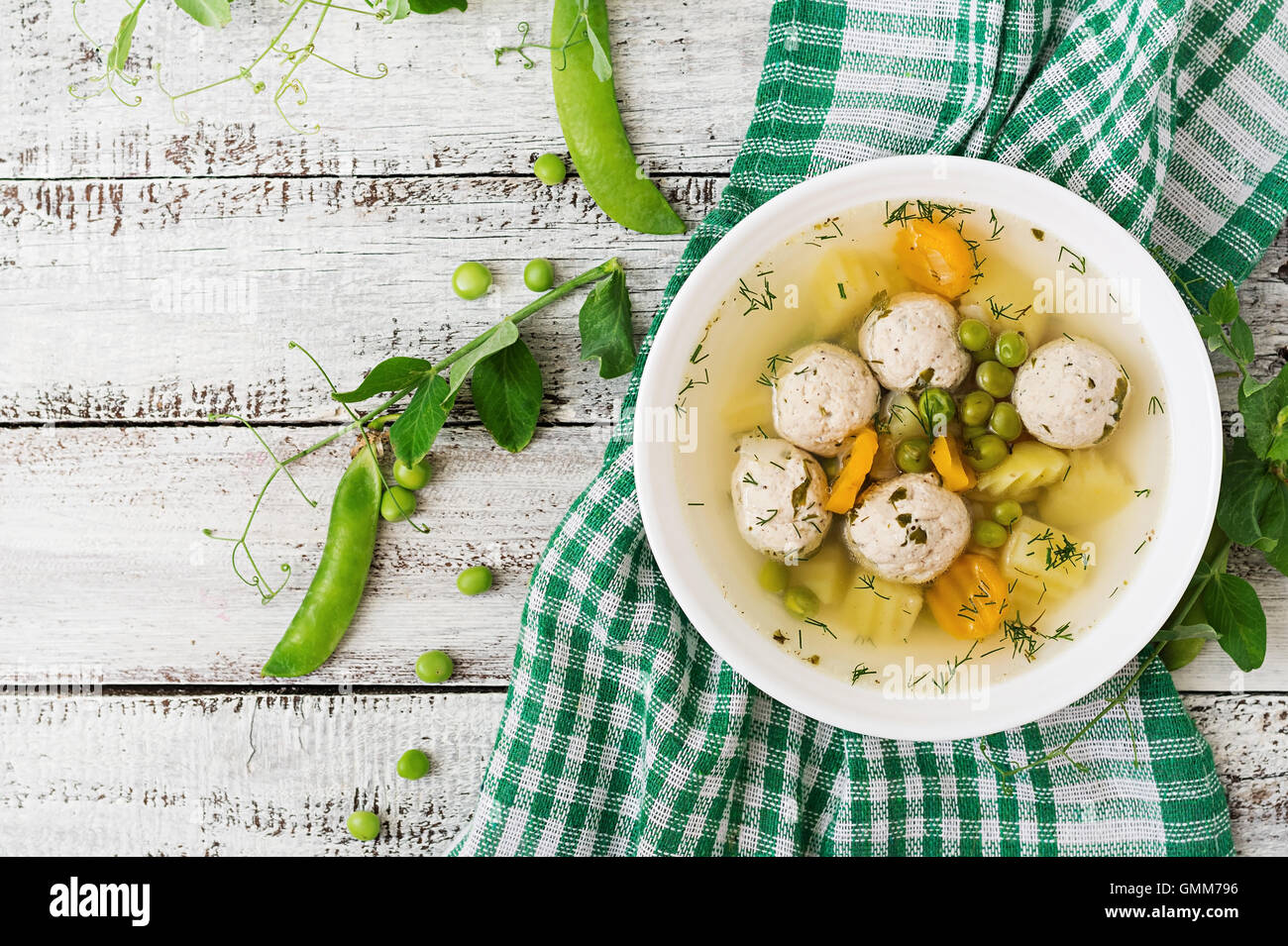 Diät-Suppe mit Hähnchen Frikadellen und grüne Erbsen in einer weißen Schüssel auf einem hölzernen Hintergrund. Ansicht von oben Stockfoto