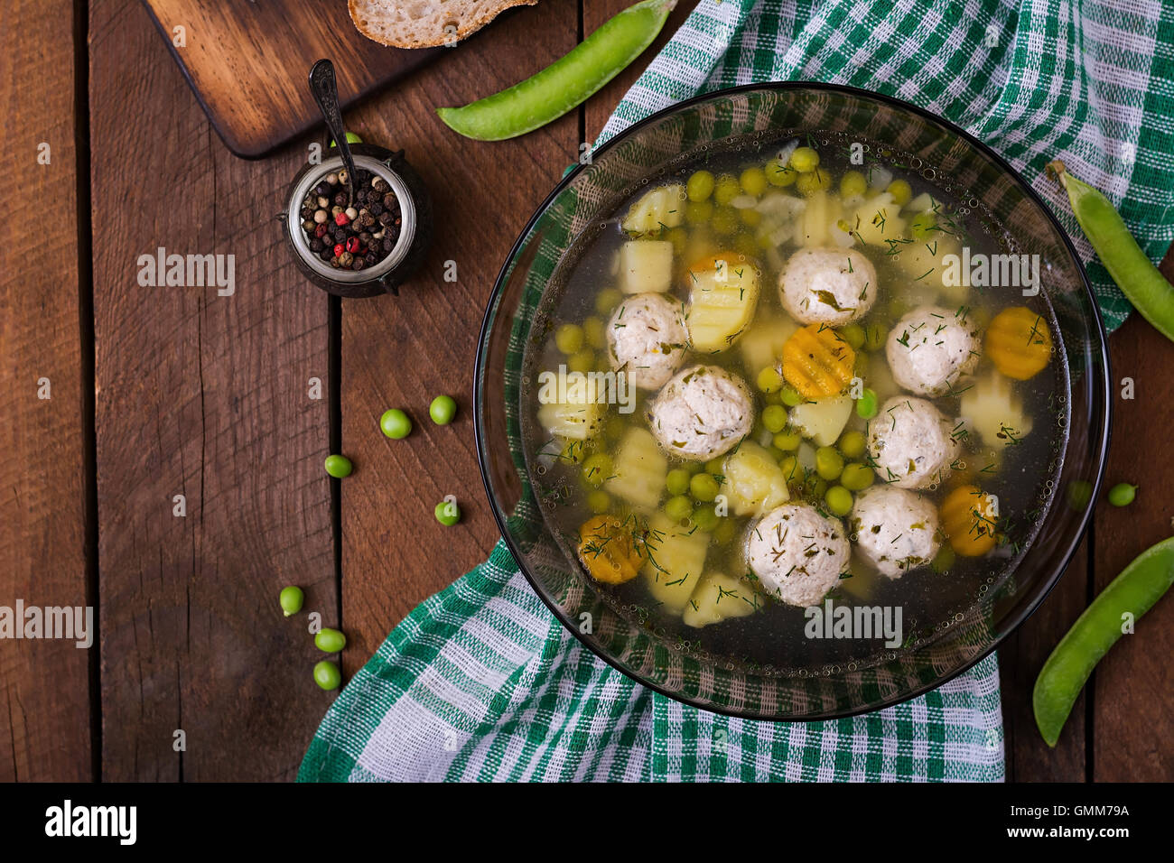 Diät-Suppe mit Hähnchen Frikadellen und grüne Erbsen in eine Glasschüssel auf einem hölzernen Hintergrund. Ansicht von oben Stockfoto