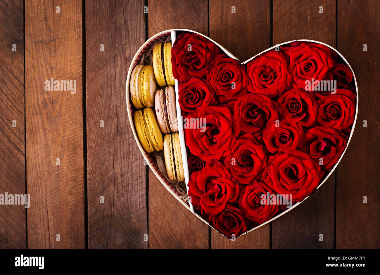 Box in der Form eines Herzens mit roten Rosen und Makronen. Geschenk zum Valentinstag. Ansicht von oben Stockfoto