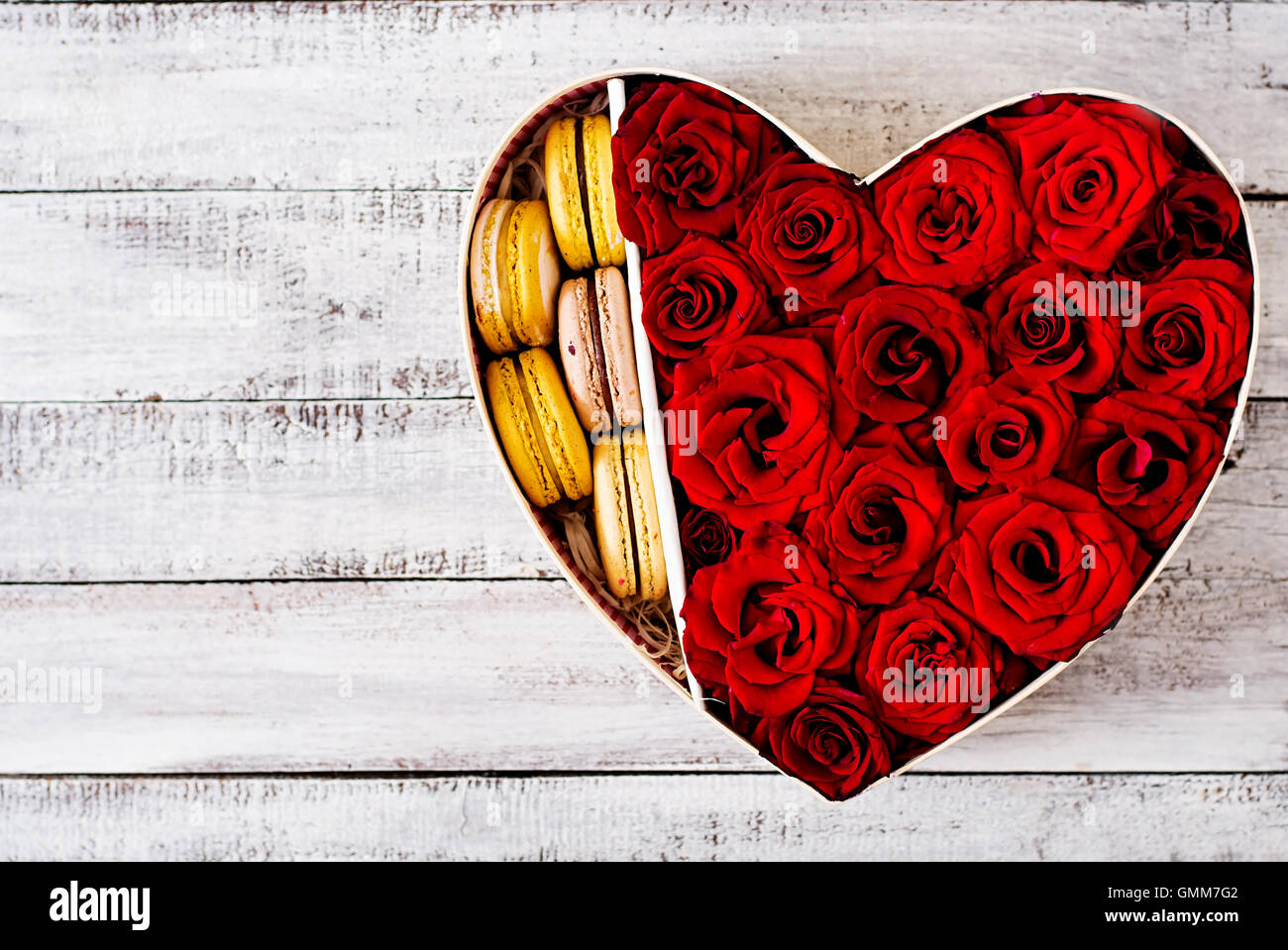 Box in der Form eines Herzens mit roten Rosen und Makronen. Geschenk zum Valentinstag. Ansicht von oben Stockfoto