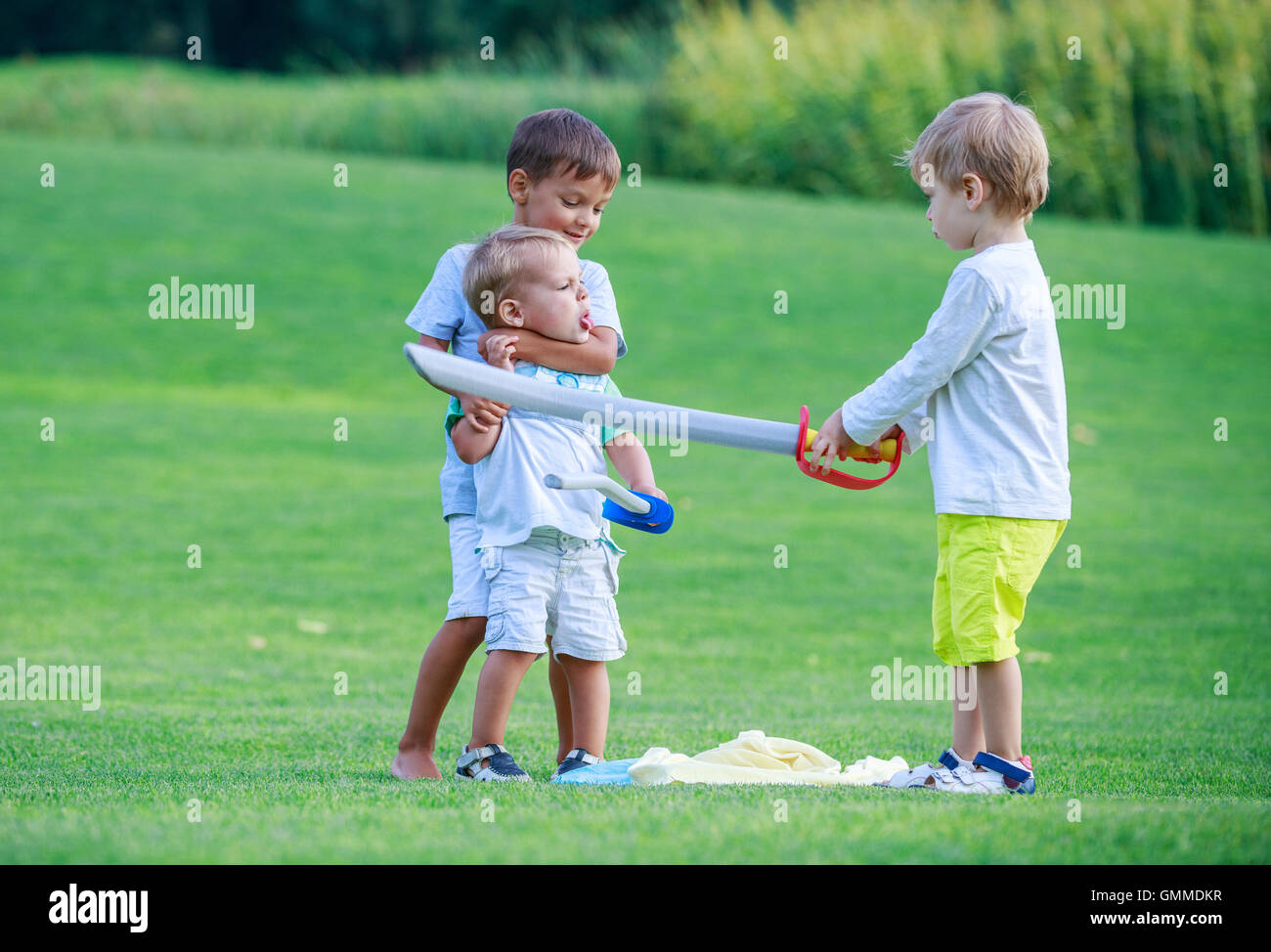 Zwei Jungen kämpfen mit Kleinkind Jungen und drohte ihm mit Spielzeug Schwert Stockfoto