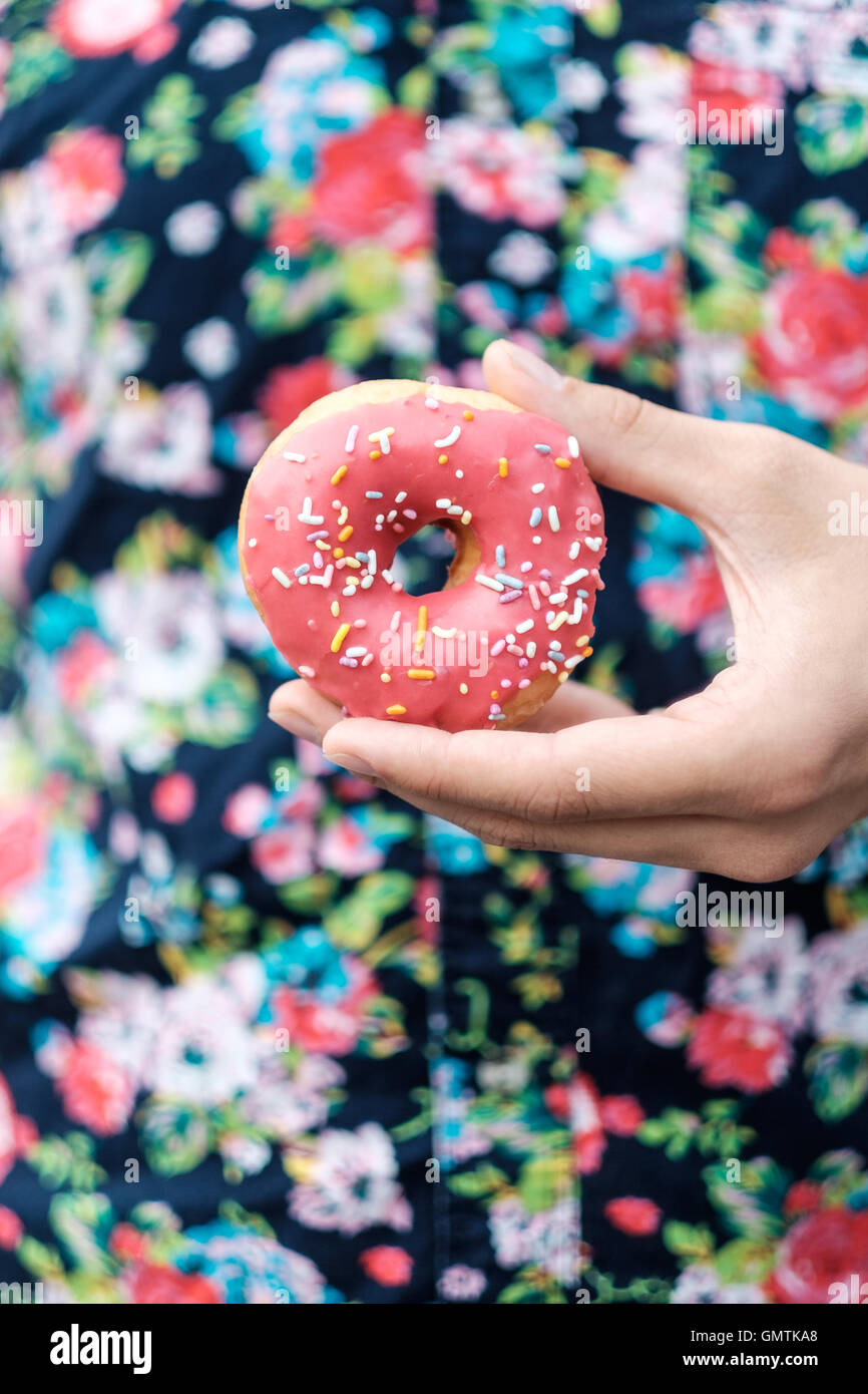 Hand, die einen rosa bestreuen Donut gegen Tastendruck florale Muster Shirt. Stockfoto