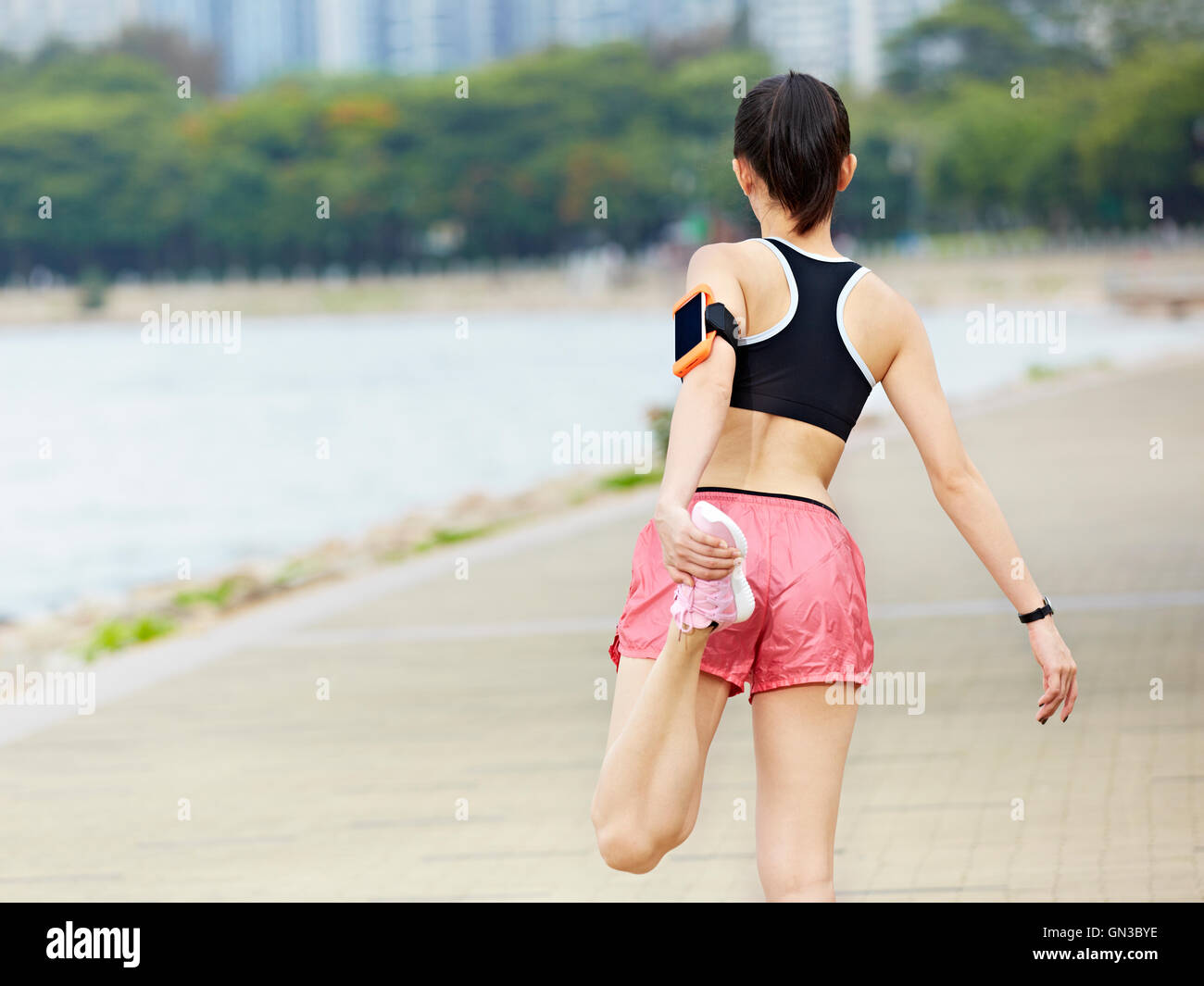 junge Asiatin Läufer Dehnung Bein in einem Stadtpark, Sicht nach hinten. Stockfoto