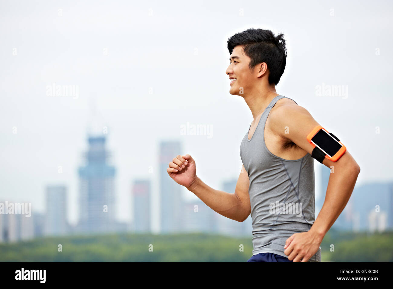 junge asiatische männliche Jogger mit Fitness-Tracker, um mit Skyline im Hintergrund läuft arm befestigt. Stockfoto