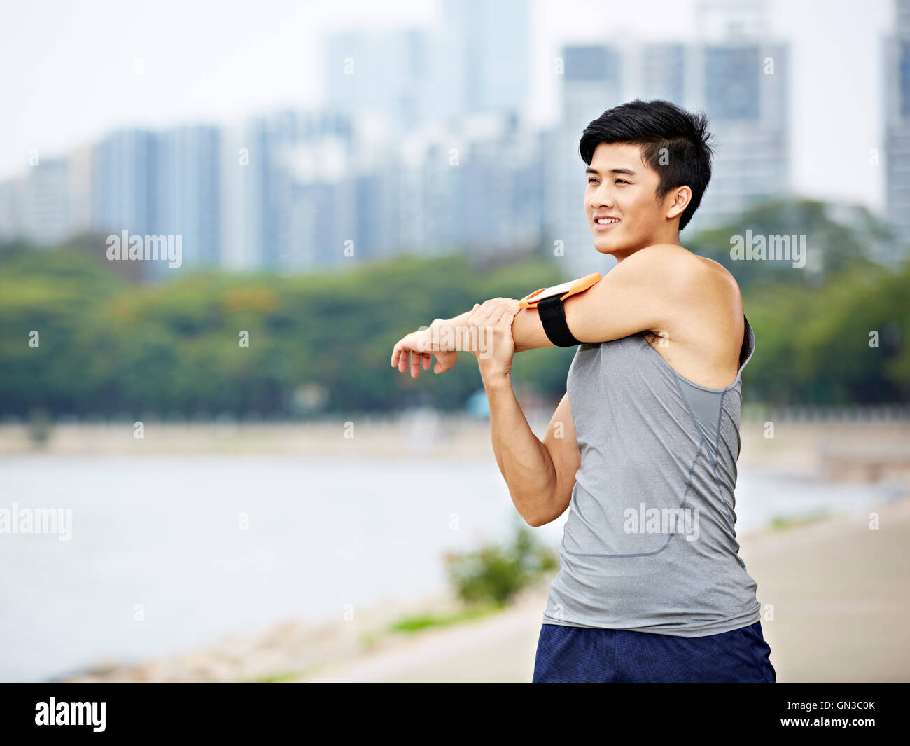 junge asiatische männliche Jogger mit Fitness-Tracker verbunden Erwärmung bis Arm durch Streckung der Arme und Oberkörper vor dem ausführen, Stadt s Stockfoto