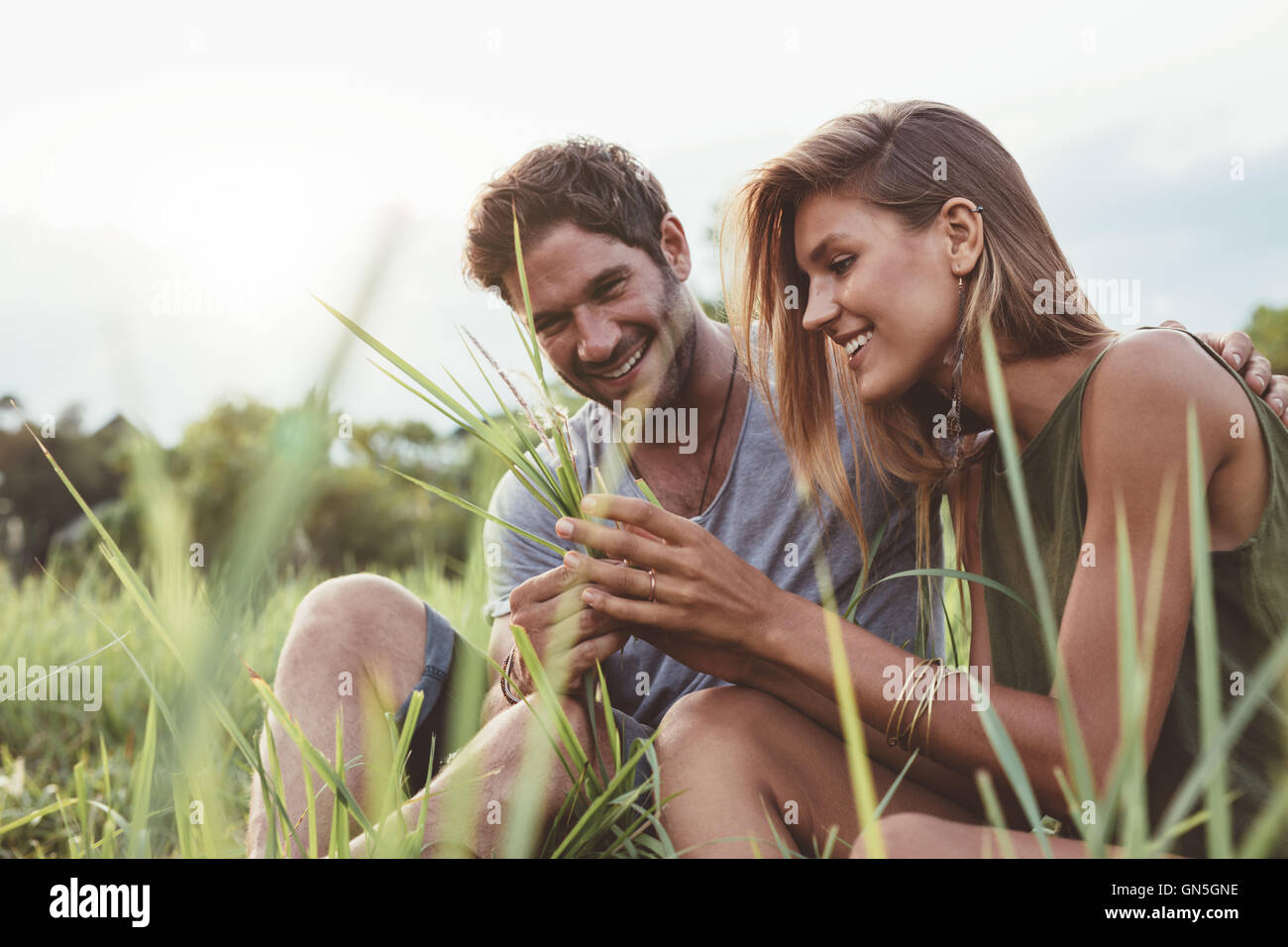 Paar in einem Feld Gras sitzen. Mann und Frau gemeinsam mit Wild grass in der hand. Stockfoto