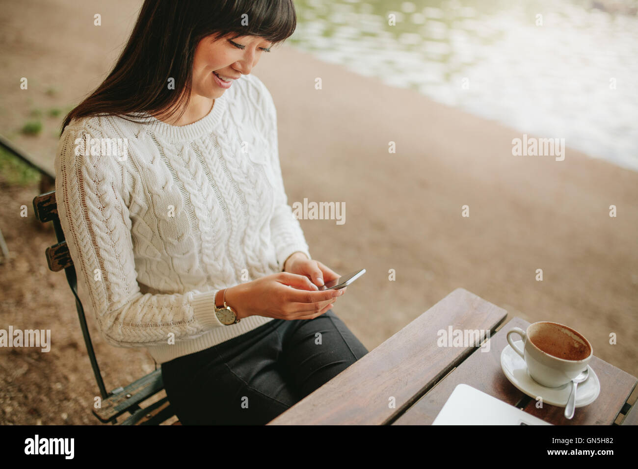 Schuss von junge Frau sitzt im Café im Freien mit Handy und lächelnd. Lesen der SMS-Nachricht auf ihr Smartphone an c weiblich Stockfoto