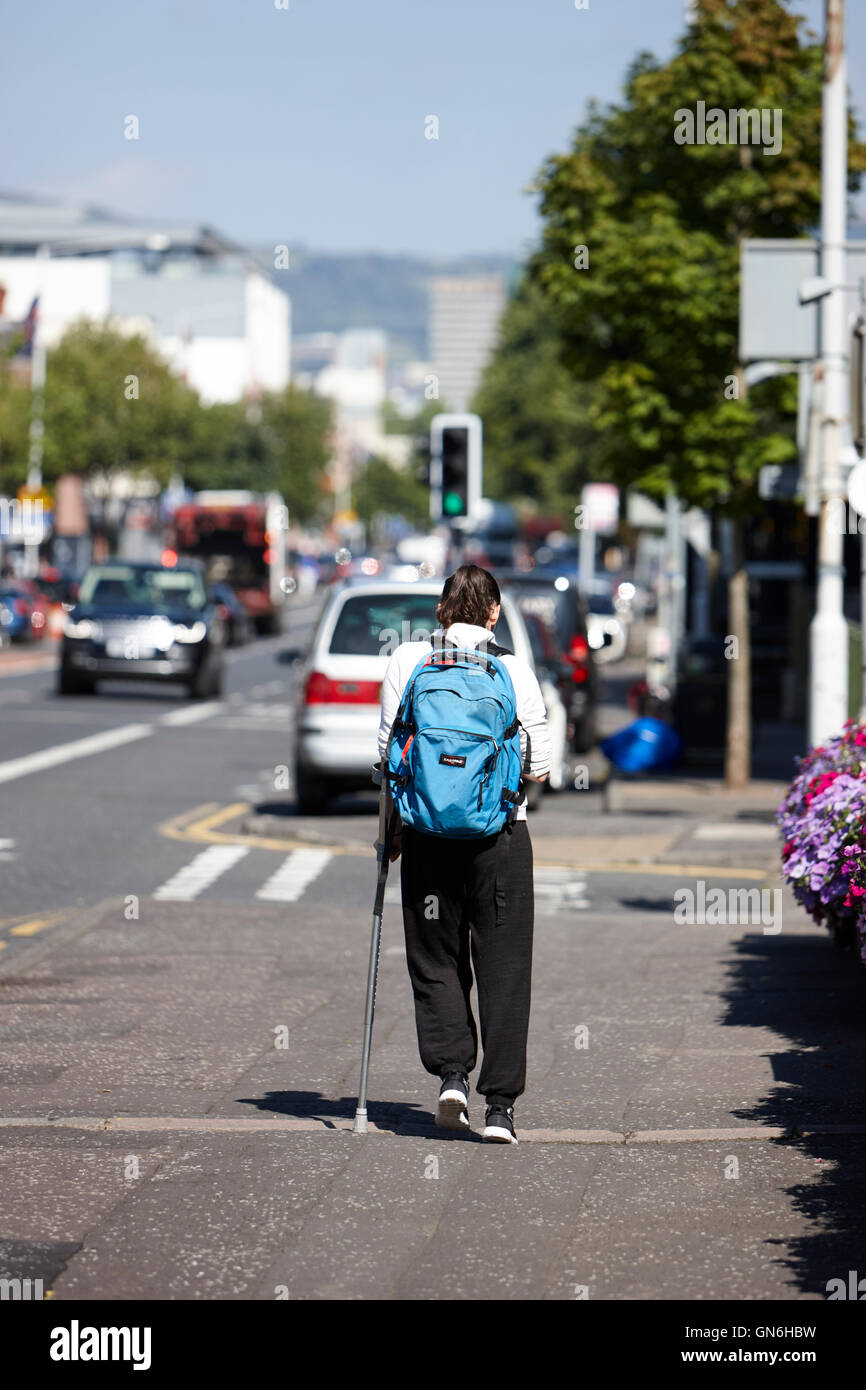 junge Frau, die mit einer einzigen Krücke Rucksack auf Vorort Straße Stockfoto