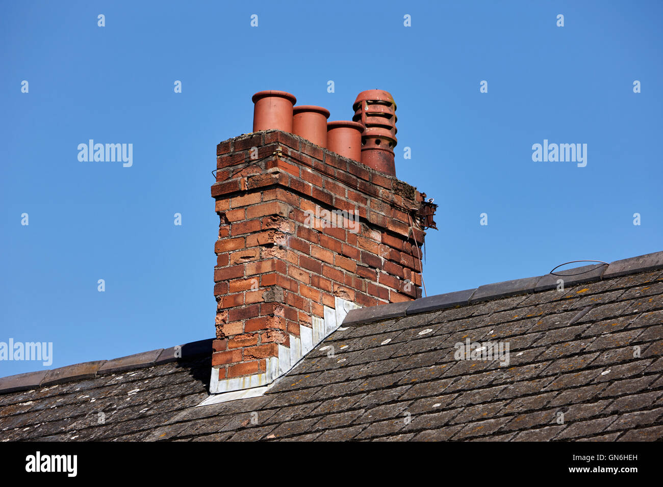 alten viktorianischen Schornstein mit Töpfen auf dem Dach aus einer Reihe von Reihenhäusern vor blauem Himmel im Vereinigten Königreich Stockfoto