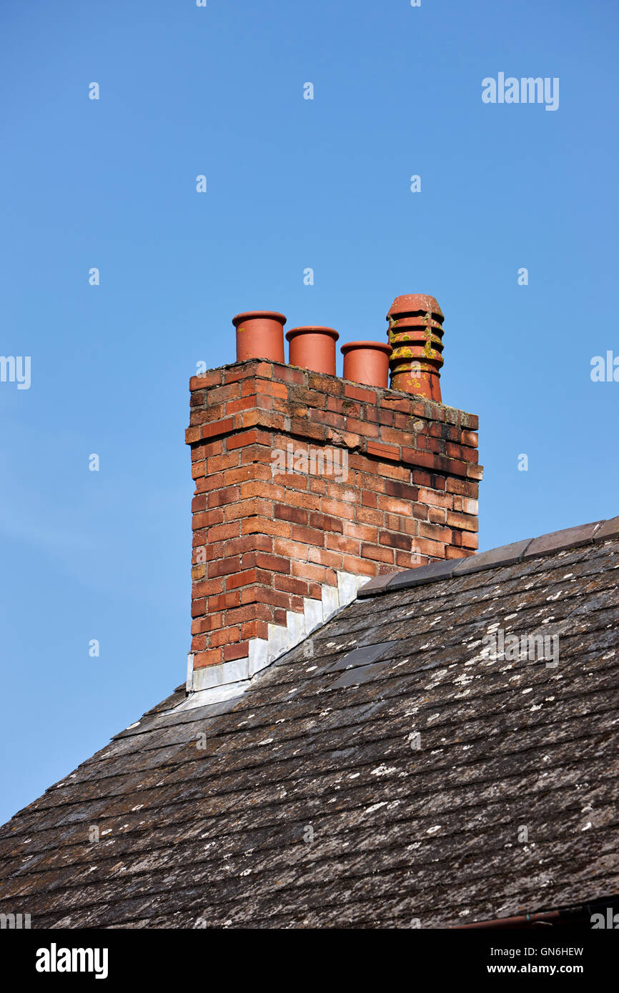 alten viktorianischen Schornstein mit Töpfen auf dem Dach aus einer Reihe von Reihenhäusern vor blauem Himmel im Vereinigten Königreich Stockfoto