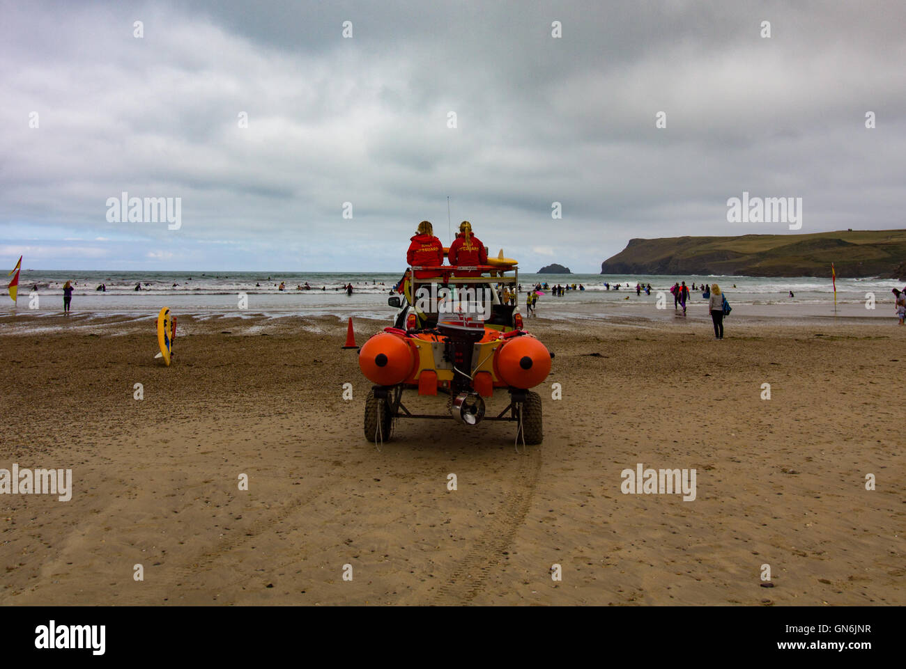 Zwei weibliche RNLI Rettungsschwimmer wachen, wie Menschen lernen zu surfen an einem kühlen Sommermorgen am Polzeath Strand, North Cornwall, UK Stockfoto