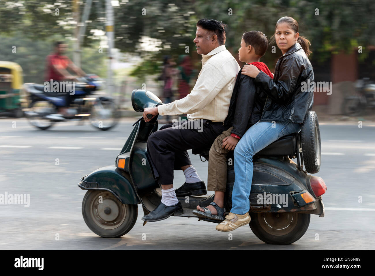 Drei auf einem Motorroller für zwei Personen auf der viel befahrenen Hauptstraße in Agra in Uttar Pradesh, Indien. Stockfoto