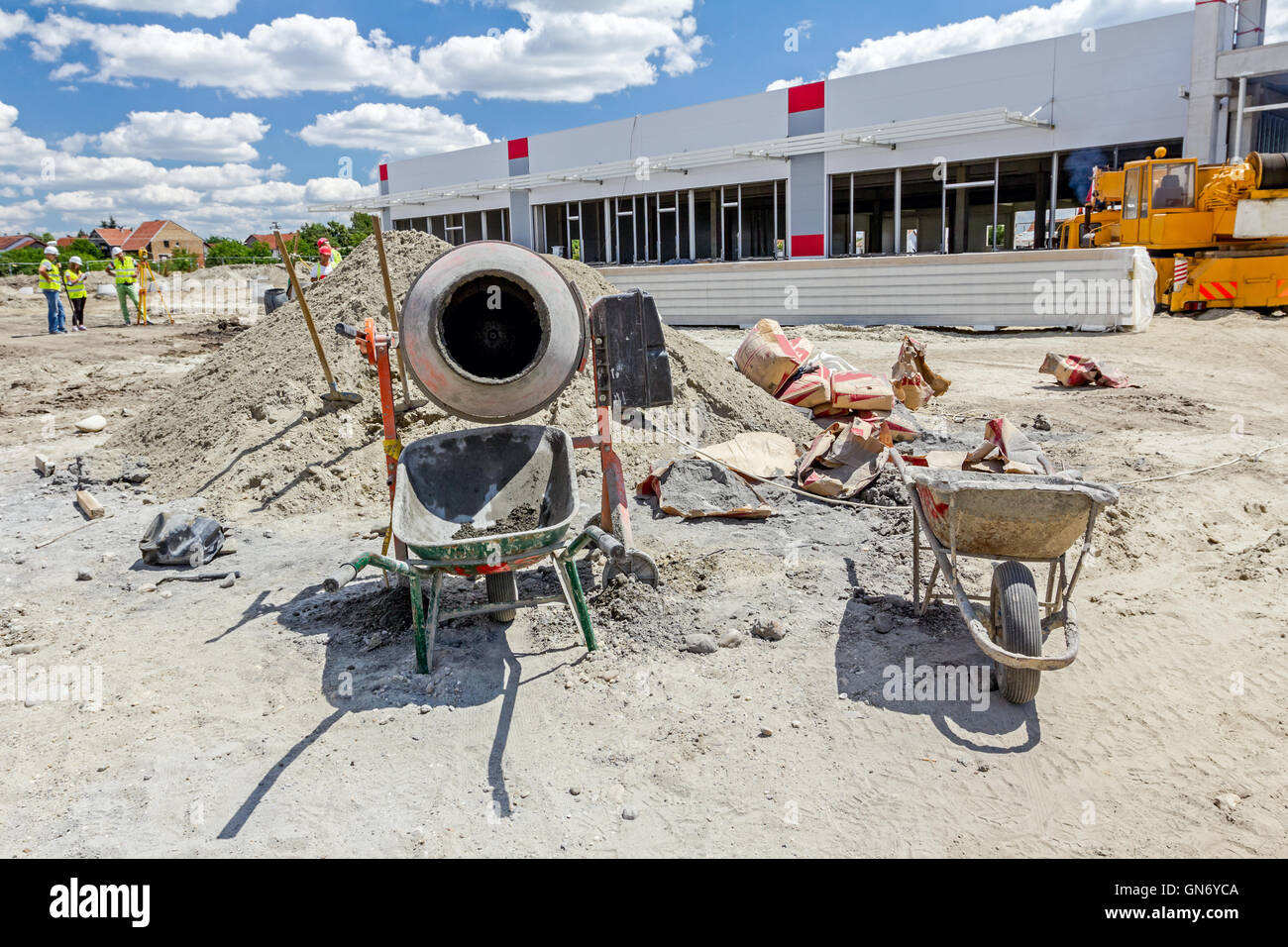 Betonmischer-Maschine ist auf Baustelle mit zwei Schubkarren, Werkzeuge, Sand und Zement Tasche. Stockfoto