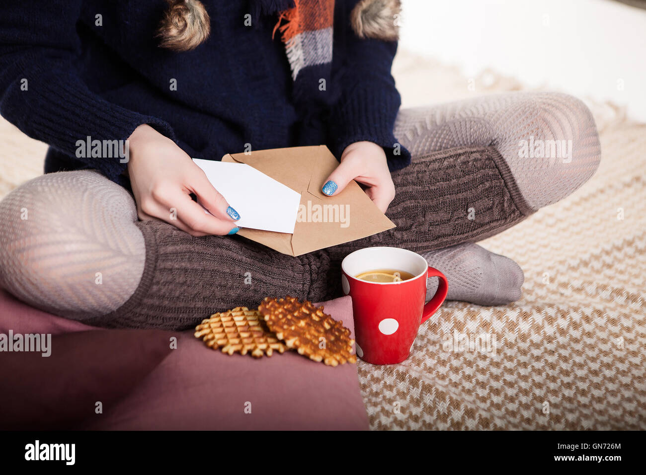 Weiche gemütliche Foto von schlanke Tan Frau in warmen Pullover auf dem Bett mit Tee in Händen, Ansicht von oben Punkt. Komposition mit warmen Plaid, Umschlag, Tasse Heißgetränk und weibliche Beine Stockfoto