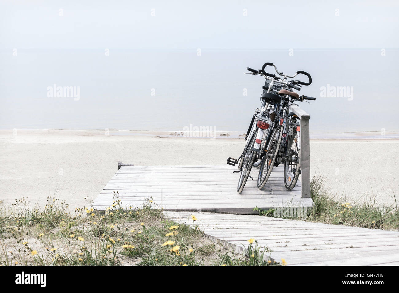 Drei Fahrräder auf hölzernen Rastplatz von leeren Strand geparkt. Entsättigt horizontal ausgerichtete Bild Stockfoto