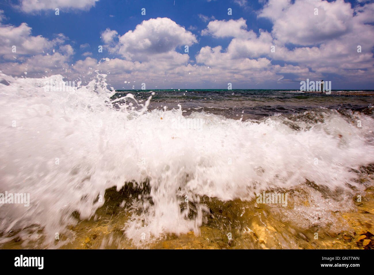 Einsamen Fischer bei Ebbe am Strand bricht eine Welle an der Küste im Vordergrund Stockfoto