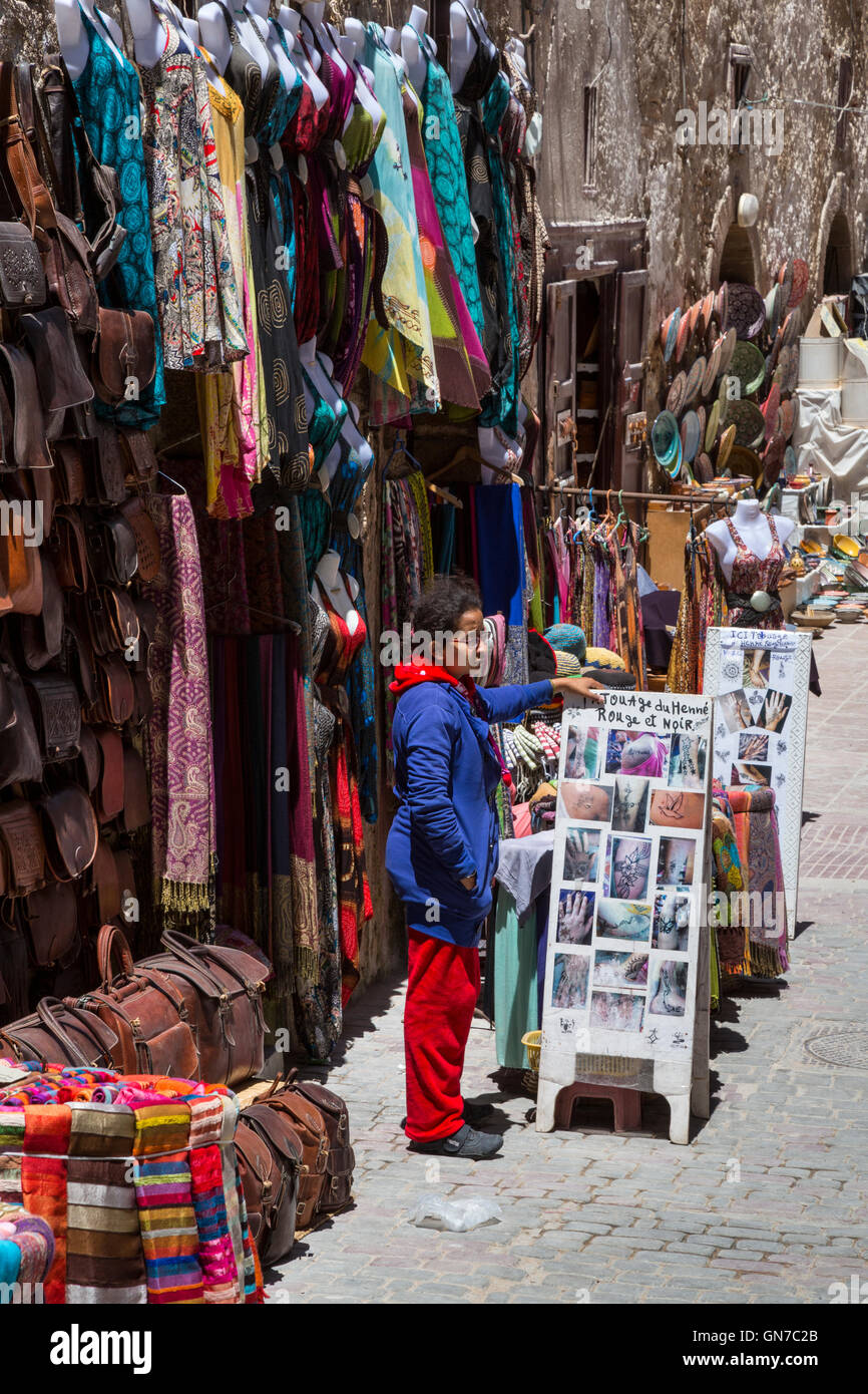 Essaouira, Marokko.  Souvenir Anbieter stehen mit einem Schild mit Henna-Tattoos, Rue De La Skala. Stockfoto