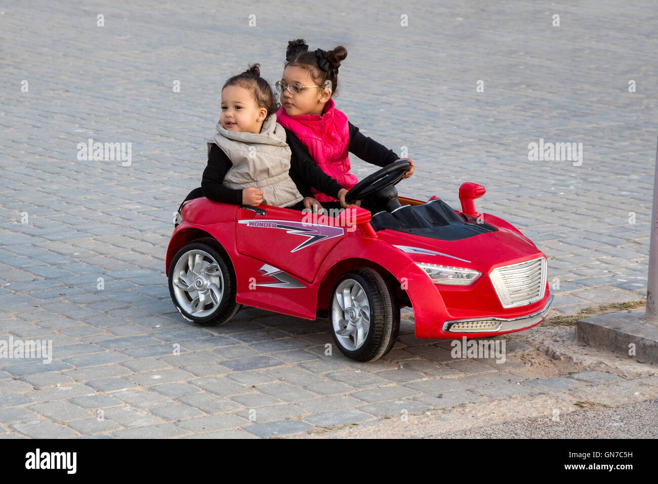 Essaouira, Marokko.  Mädchen reiten in Spielzeugauto in den Platz Moulay Hassan. Stockfoto
