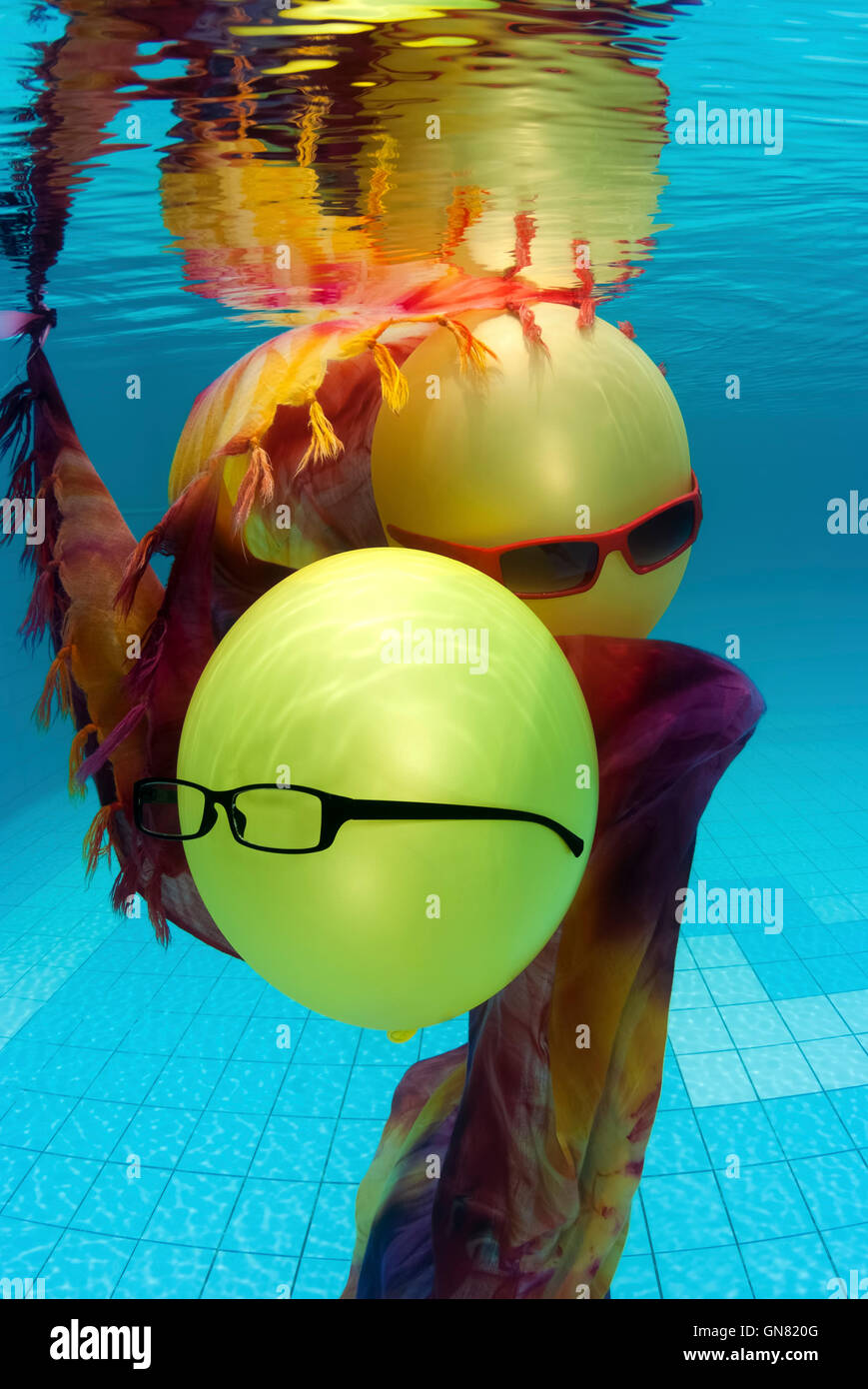 Bunte Party Ballon mit Sonnenbrille unter Wasser in einem Schwimmbad, was eine Atmosphäre der Feier, Freude und Glück. Stockfoto