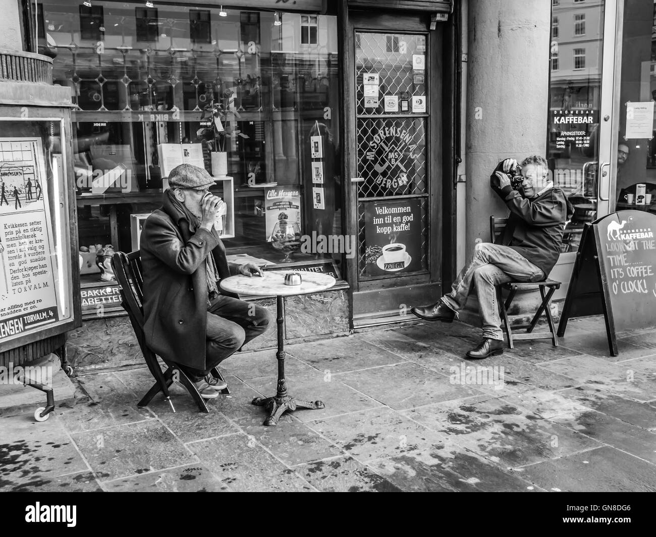 Eine Erwachsene männliche Model seine Tasse Kaffee genießen, während ein Fotograf fotografieren sein Porträt vor einer Kaffee-Bar. BW-Version. Stockfoto