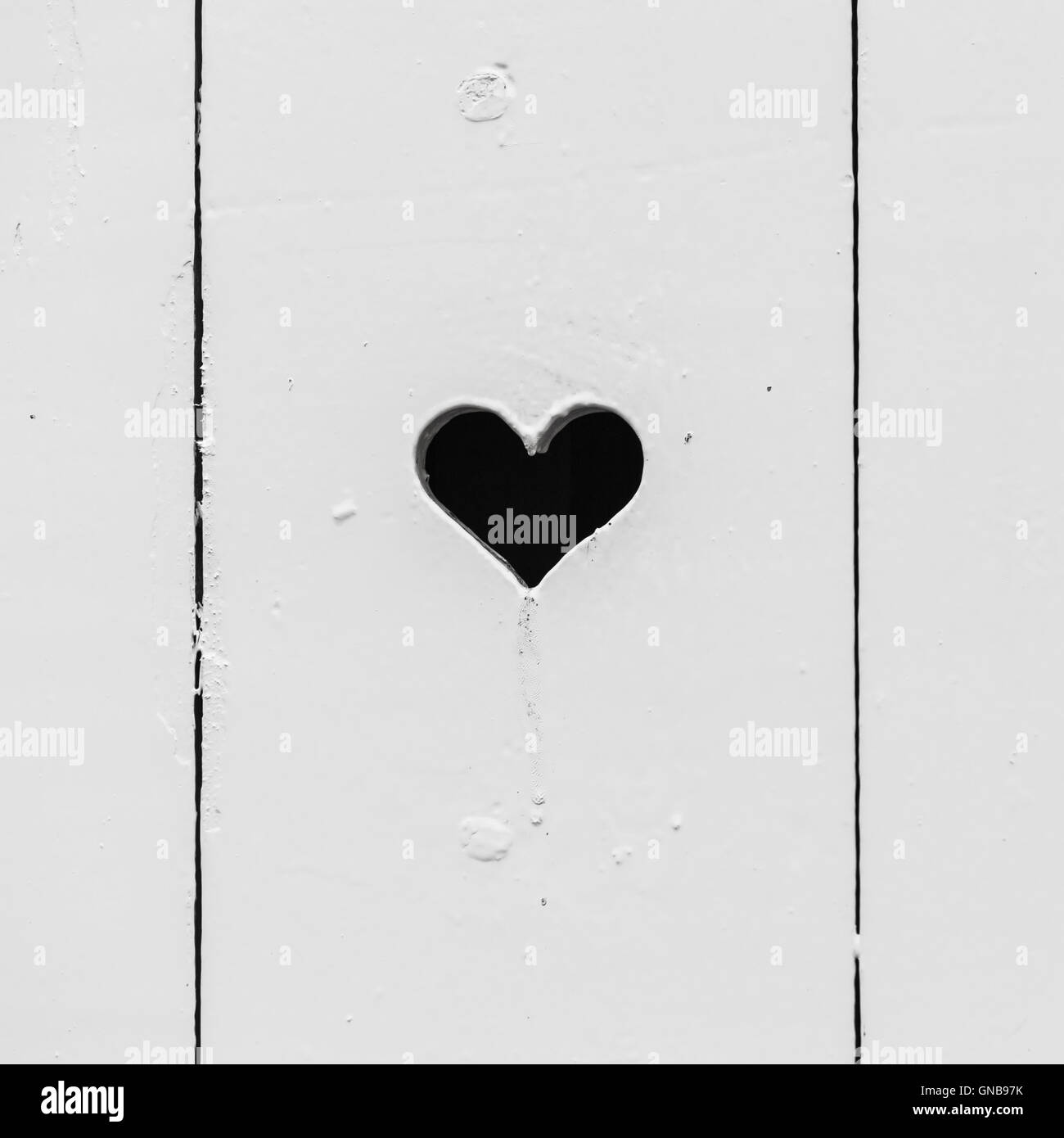 Schwarzes Loch im weißen Holzwand, quadratische Hintergrundtextur Foto in Herzform Stockfoto